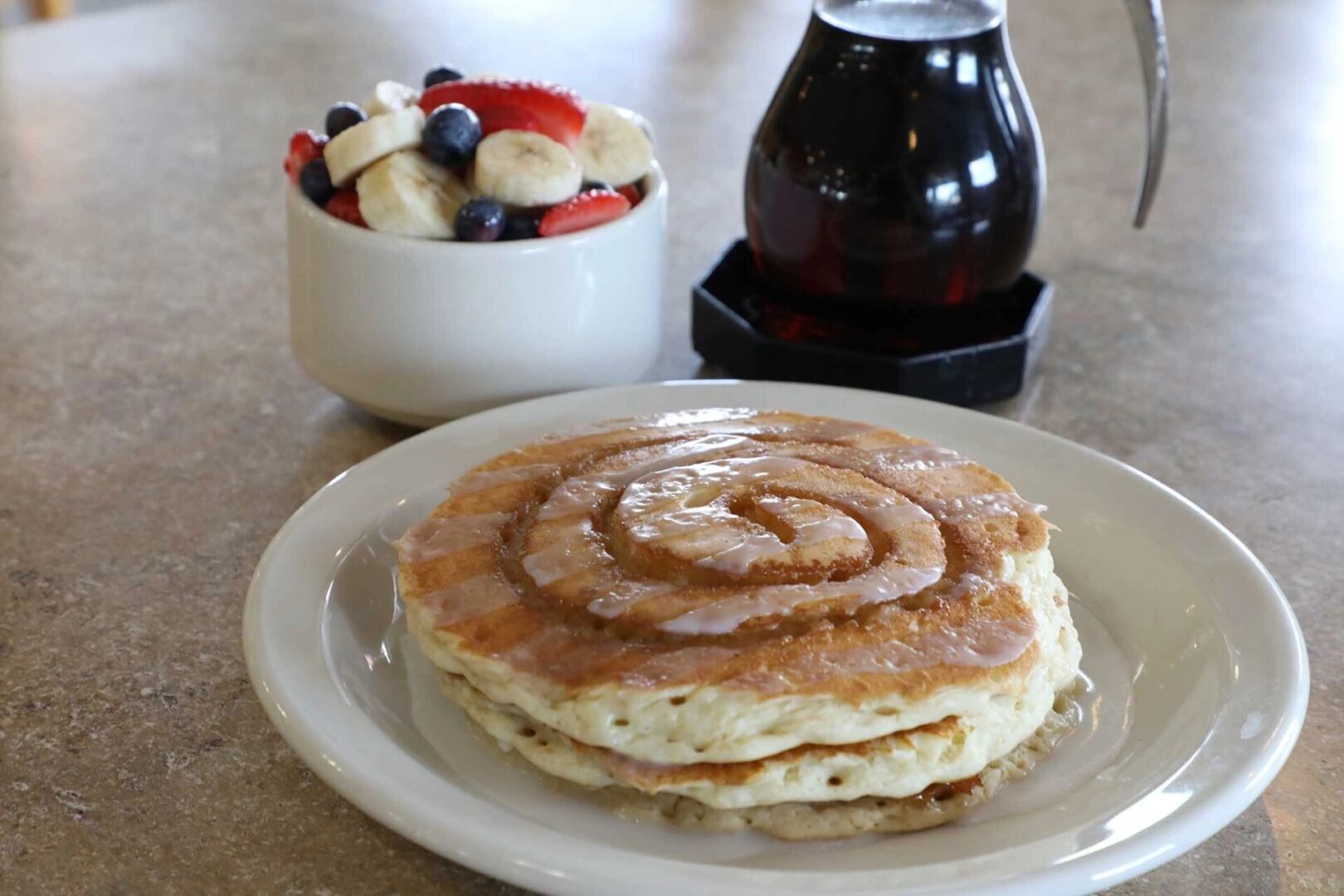 A plate of pancakes with syrup and fruit.